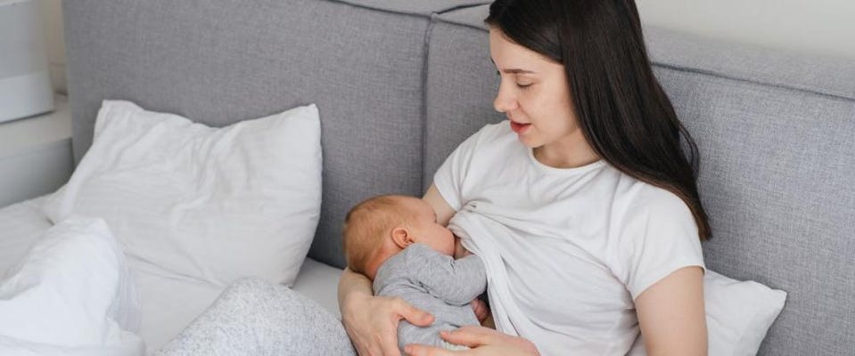 Mom breastfeeding newborn on bed