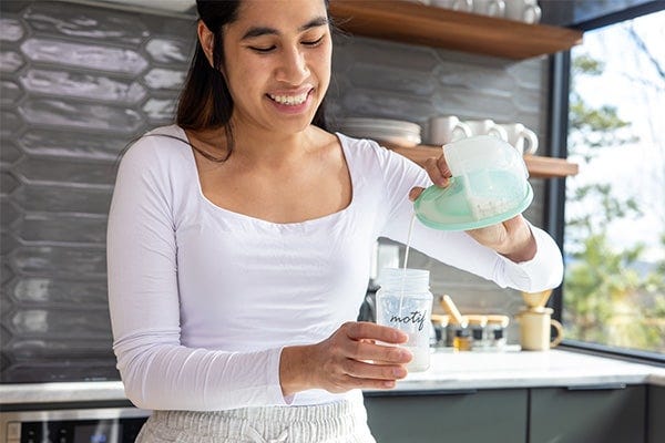 Mom pouring milk out of the milk spout of the Motif Aura Glow™ Wearable Breast Pump