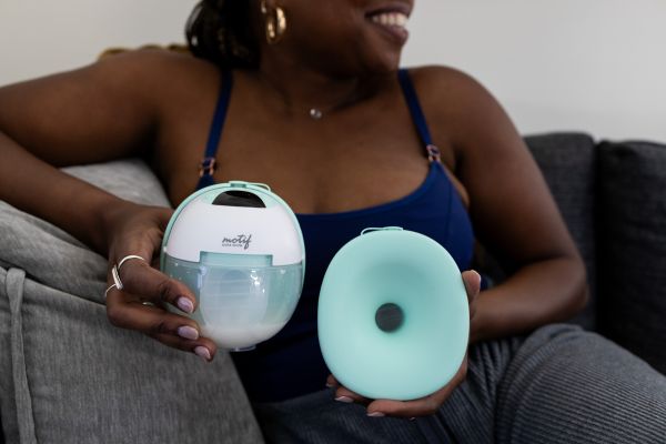 Breastfeeding mom holding the Motif Aura Glow wearable breast pump 