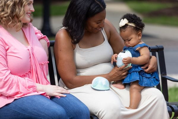 Breastfeeding mom outside with her baby holding the Motif Aura Glow Wearable Breast PUmp