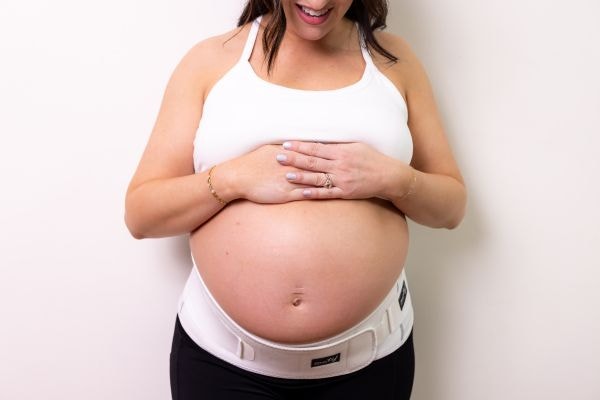 pregnant mom holding her belly while wearing Motif Medical's Pregnancy Back Brace