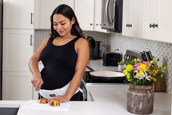 mom wearing motif medical's pregnancy support band cutting an apple.