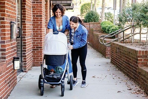 two moms walking outside laughing while walking their baby. one mom is wearing motif medical pregnancy support leggings