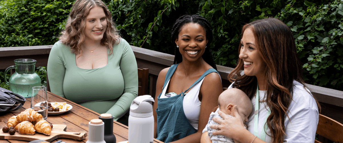 Celebrating Individuality: Embracing Your Unique Pumping Journey Two Moms are walking outside with a baby basket in one of the mother's hand. They are both laughing. One mom is pregnant happily touching her belly. The other mom is using her Motif Aura hands-free breastpump.