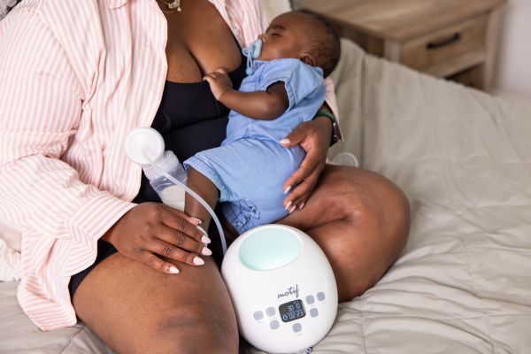 Mom holding baby while pumping with the Motif Luna Double Electric Breast Pump