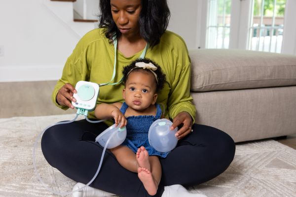 mom holding her baby while pumping with the Motif Roam Breast Pump With Breast Milk Collection Cups